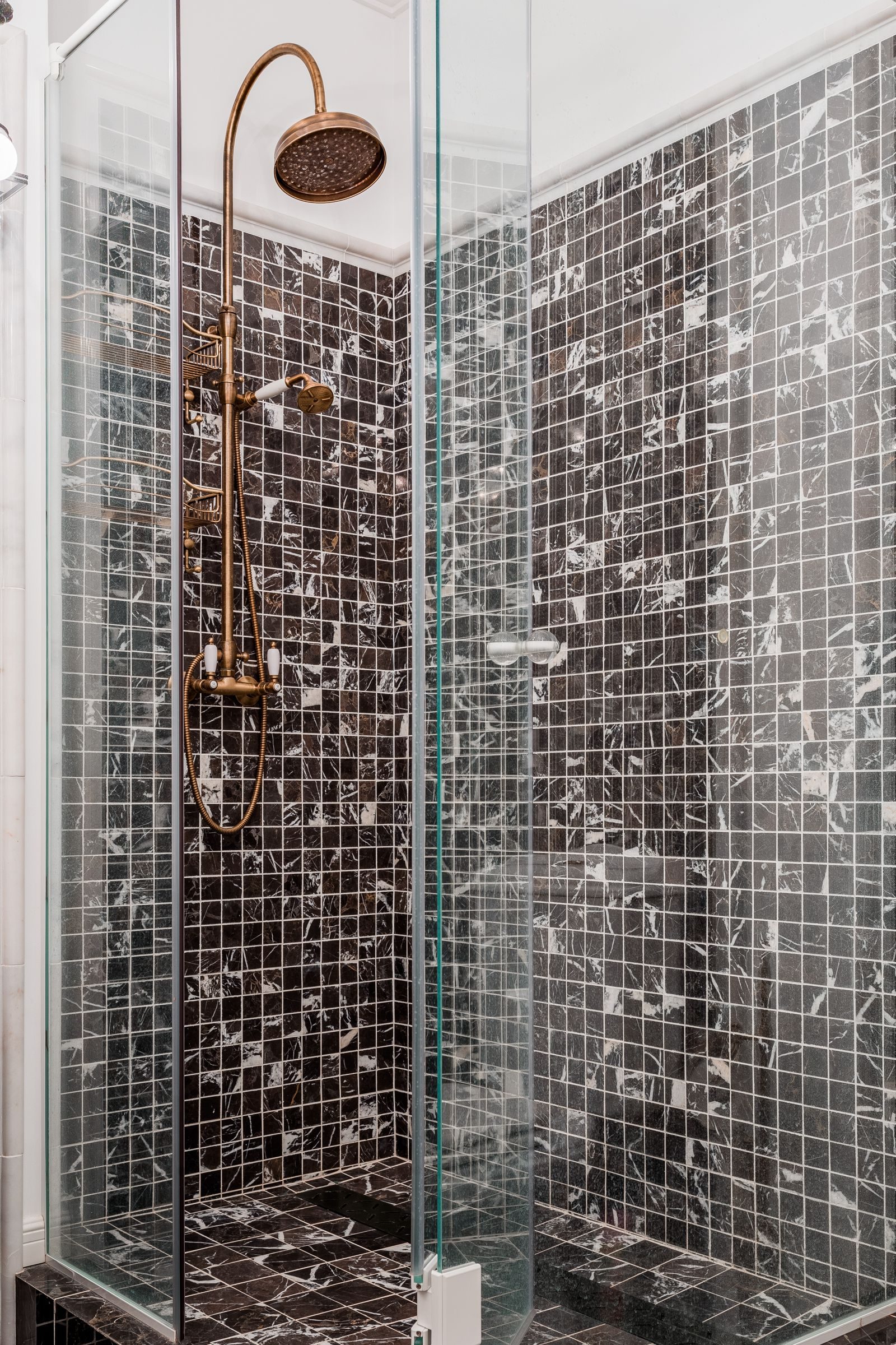 A walk-in shower with brass fittings and mosaic tiles